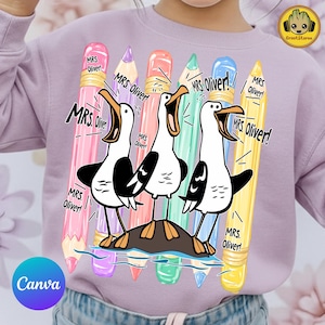 May include: A light purple sweatshirt featuring a graphic print of three seagulls standing on a rock, surrounded by five colorful pencils in pink, purple, orange, green, and yellow. The text "MRS. OLIVER!" is repeated multiple times around the birds.