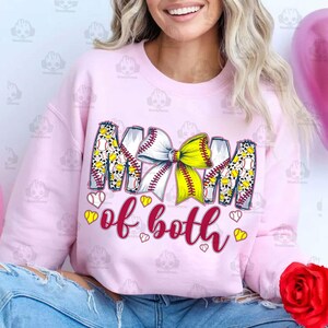 May include: Pink sweatshirt with the text "Mom of both" in maroon. The text is surrounded by a design of baseballs, a yellow and white bow, and leopard print.
