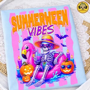 Peut inclure: Un t-shirt bleu clair avec une illustration d'un squelette portant un chapeau de paille et des lunettes de soleil, assis dans une bouée flamant rose. Le motif inclut le texte orange SUMMERWEEN VIBES, des citrouilles, des bougies et des chauves-souris.