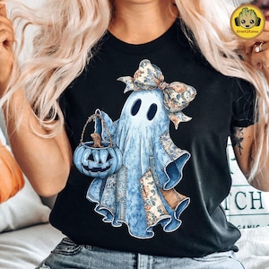 May include: Black t-shirt featuring a light blue ghost illustration with a floral bow and patches. The ghost holds a blue jack-o'-lantern bucket. The design has a vintage, patchwork aesthetic, perfect for Halloween.