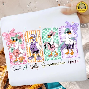 May include: A white t-shirt featuring a graphic of four geese in summer and Halloween-themed outfits, including swimsuits, snorkels, and surfboards, with the text Just A Silly Summerween Goose printed in black script at the bottom of the design.
