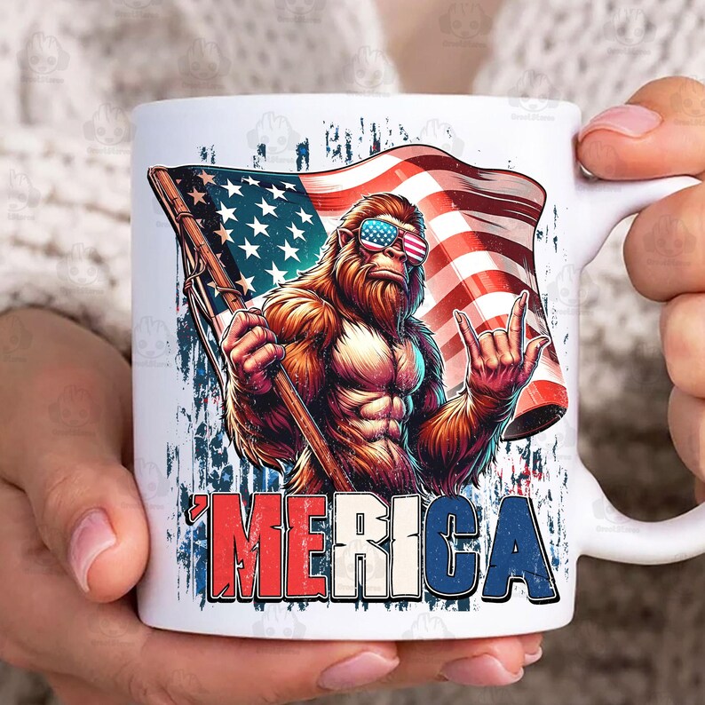 May include: White ceramic mug featuring a patriotic design. The mug displays a muscular Bigfoot character wearing sunglasses with an American flag design, holding a flag, and flashing a rock-on hand gesture. The word 'MERICA' is printed in red, white, and blue.