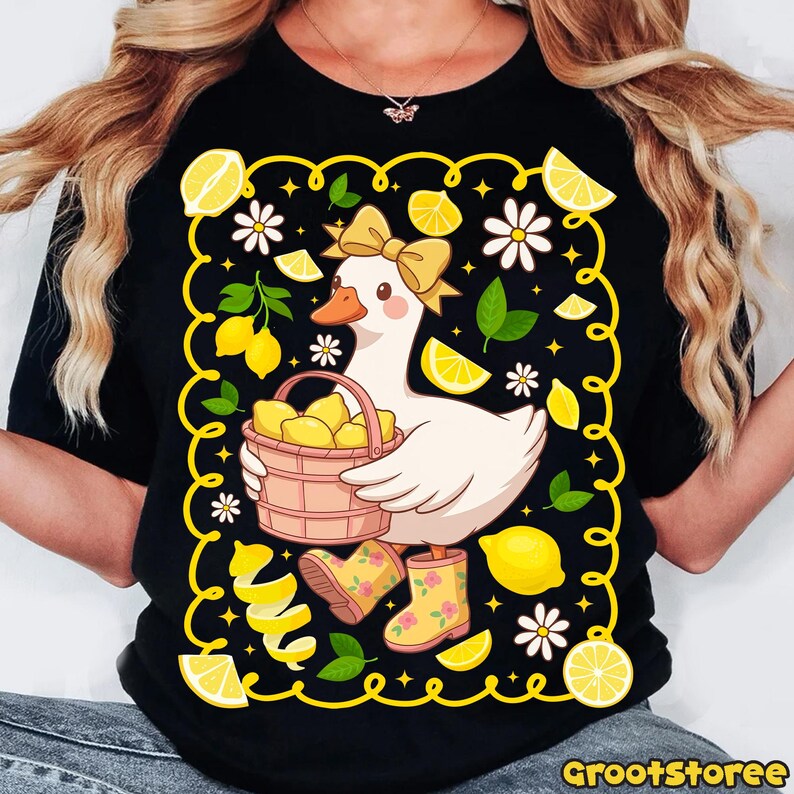 May include: Black t-shirt featuring a cartoon goose with a yellow bow, holding a basket of lemons. The design includes lemons, daisies, and lemon peel accents, with yellow rain boots. The shirt has the text "GrootStoree" at the bottom.