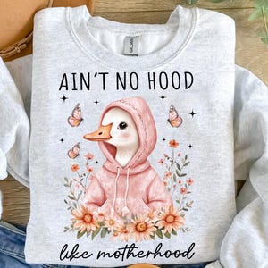 May include: A gray sweatshirt with a white duck wearing a pink hoodie and the text "Ain't no hood like motherhood" with flowers and butterflies.