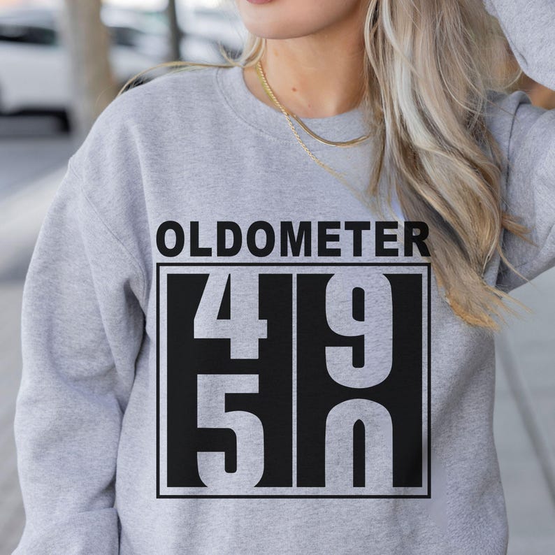 May include: A light gray sweatshirt with the word "OLDOMETER" above a black rectangle containing the numbers "49" and "50". The sweatshirt is a casual style.
