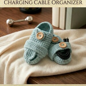 May include: Two light blue handmade crochet charging cable organizers featuring round wooden buttons. The text HANDMADE CROCHET CHARGING CABLE ORGANIZER and INSTANT DOWNLOAD HIGH QUALITY is visible at the top and bottom of the image.