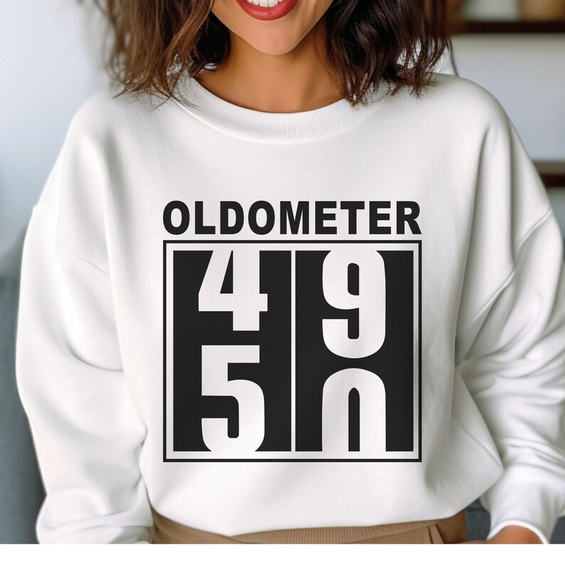 May include: White sweatshirt with the word "OLDOMETER" above a black rectangle containing the numbers "49" and "50" in white. The sweatshirt is a crew neck style.
