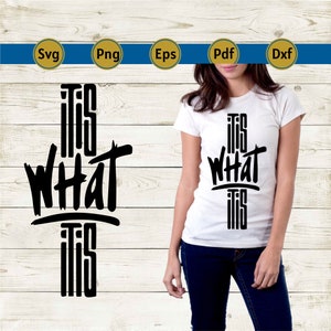 May include: White t-shirt with the phrase "IT IS WHAT IT IS" in bold black lettering. The text is vertically aligned and centered on the shirt. The shirt is being worn by a person.