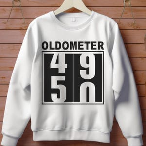 May include: White sweatshirt with the text "OLDOMETER" above a black rectangle containing the numbers "49" and "50" in a bold, sans-serif font. The sweatshirt has a crew neck and long sleeves.