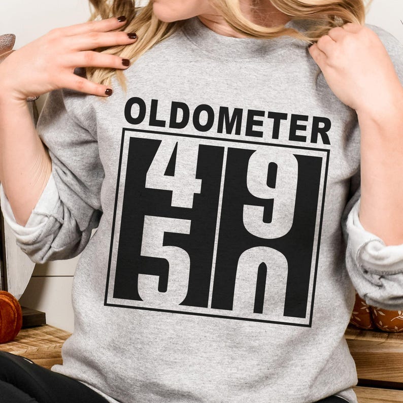 May include: A gray sweatshirt with the word "OLDOMETER" above a black and white graphic displaying the numbers "49" over "50". The sweatshirt is a casual style.