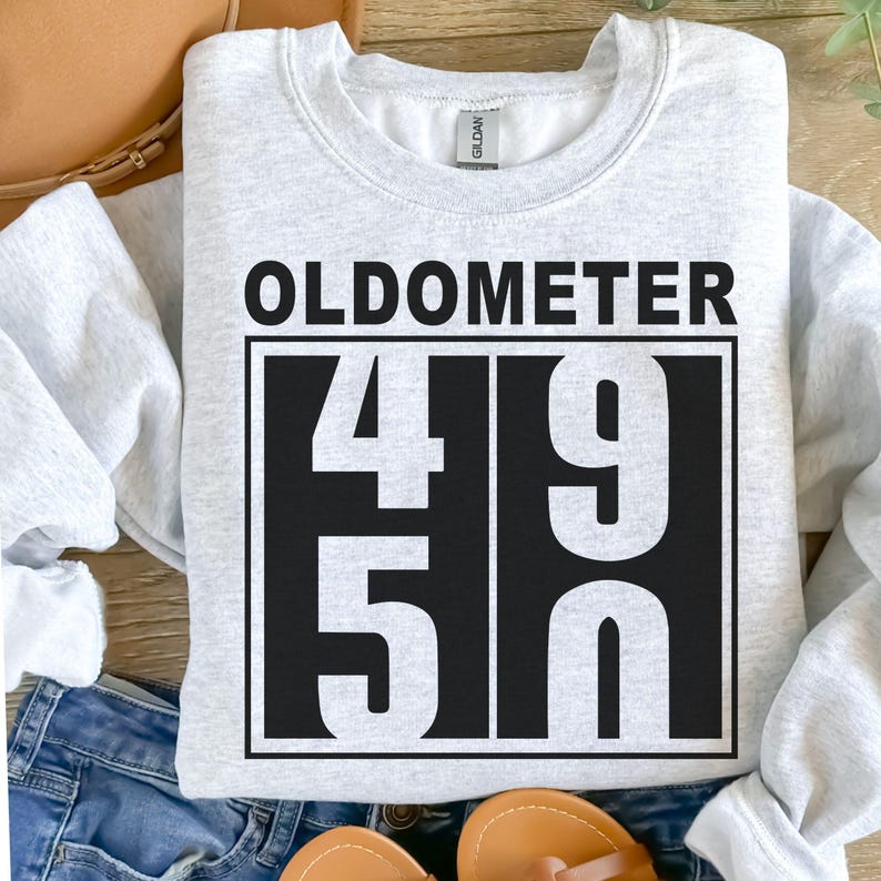 May include: A light gray sweatshirt with the word "OLDOMETER" above a black rectangle containing the numbers "49" and "50". The sweatshirt is a casual style.
