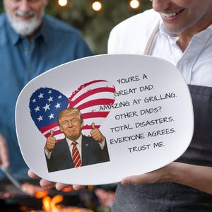 May include: White oval platter with a graphic of a smiling man giving a thumbs up, with an American flag heart and text that reads "YOU'RE A GREAT DAD. AMAZING AT GRILLING. OTHER DADS? TOTAL DISASTERS. EVERYONE AGREES. TRUST ME."