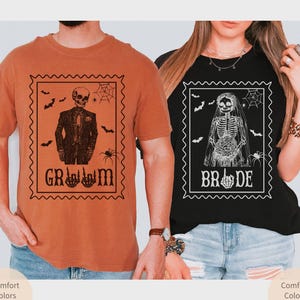May include: Two t-shirts, one orange and one black, featuring skeleton designs within postage stamp frames. The orange shirt says "Groom" and the black shirt says "Bride". Bats, spiders, and cobwebs decorate the frames. The shirts are part of a Halloween or wedding theme.