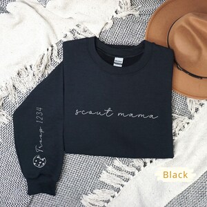 May include: Black sweatshirt with the text "scout mama" in white script on the front. The left sleeve has a white outline of a cookie with the text "Troop 1234" on it.