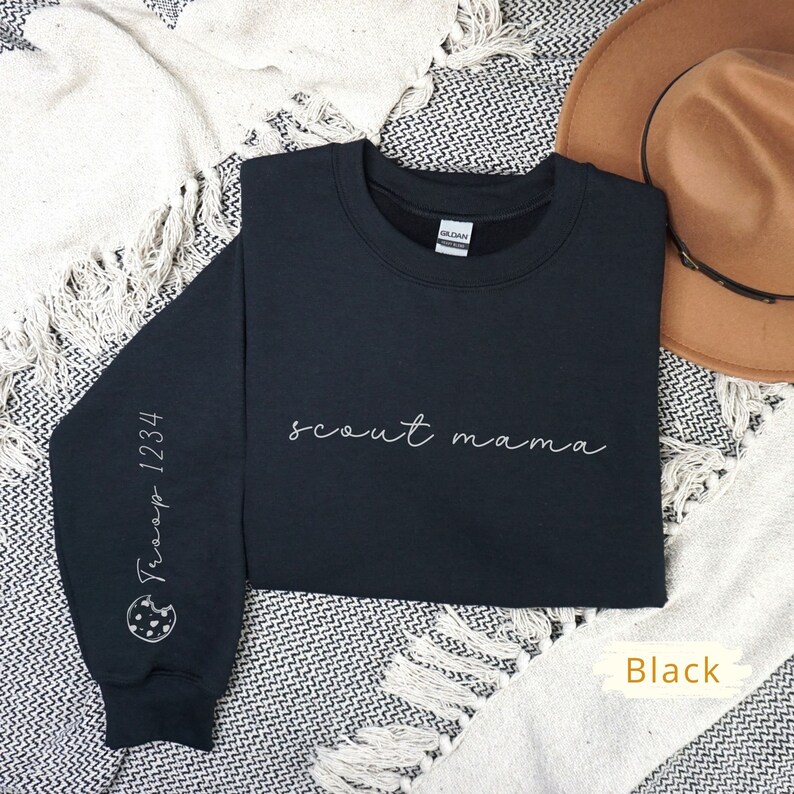 May include: Black sweatshirt with the text "scout mama" in white script on the front. The left sleeve has a white outline of a cookie with the text "Troop 1234" on it.