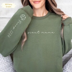 May include: A green sweatshirt with the text "scout mama" on the front and a cookie graphic with the text "1234-doors" on the sleeve.