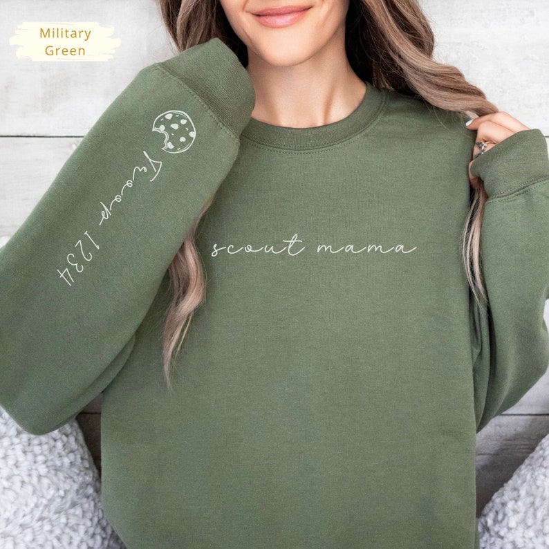 May include: A green sweatshirt with the text "scout mama" on the front and a cookie graphic with the text "1234-doors" on the sleeve.