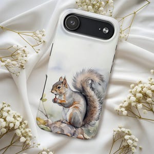 Op de afbeelding: Een wit en zwart telefoonhoesje met een aquarel illustratie van een grijze eekhoorn die een noot vasthoudt. De eekhoorn zit op een rots met een pluizige staart. De hoes heeft een camera-uitsparing en een zwarte rand.