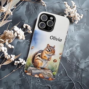 May include: White phone case featuring a watercolor illustration of a chipmunk holding a nut, with the name "Olivia" in black text. The chipmunk is brown, white, and black, sitting on a rock with scattered nuts. The case has a glossy finish.