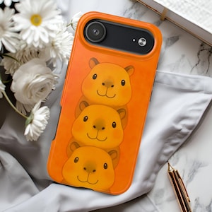 May include: An orange smartphone case featuring a vertical stack of three cartoon capybara illustrations. The case has a black camera cutout at the top, and the capybaras are depicted with simple facial features, round ears, and a warm, solid orange background.