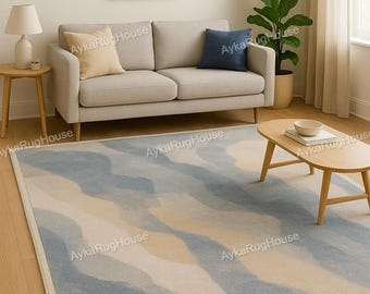 May include: A rectangular area rug with a wavy pattern in shades of blue and beige. The rug is placed on a hardwood floor, with a light-colored sofa, pillows, and a wooden coffee table in the background. The rug's dimensions are approximately 8 x 10 feet.
