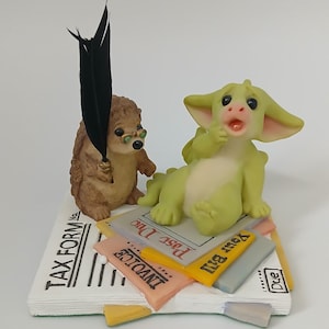 Può includere: Una statuetta di drago verde con un'espressione sorpresa è seduta su una pila di carte con le parole "Your Bill", "Invoice" e "Past Due". Una statuetta di riccio marrone con gli occhiali tiene una penna di piuma nera.