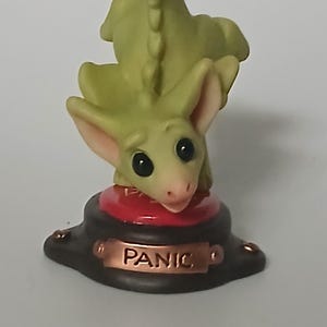 May include: A green dragon figurine with large ears and a long tail, standing on a red button labeled "PANIC".
