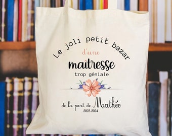 May include: A white tote bag with the text "Le joli petit bazar d'une maîtresse trop géniale de la part de Mathéo 2023-2024" printed on it. The text is surrounded by a floral design.