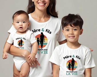Op de afbeelding: Witte t-shirts en een babyrompertje met een afbeelding van een silhouet van een ouder en kind tegen een cirkelvormige zonsondergang. De tekst Mère & fils en Une équipe pour LA VIE staat in zwarte en blauwgroene letters op de kledingstukken.