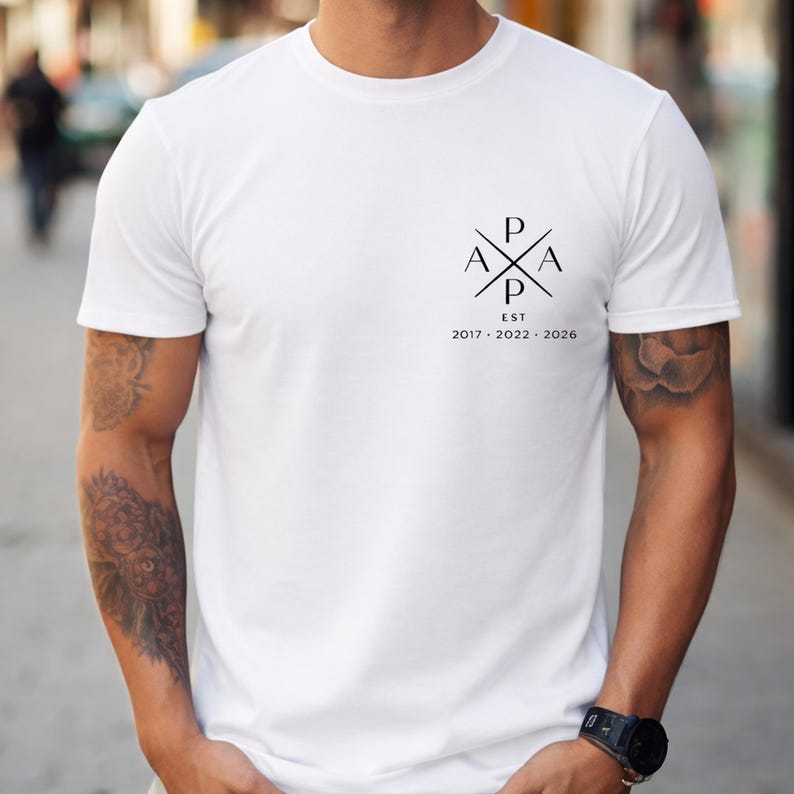 May include: White crew neck t-shirt with a black graphic on the upper left chest. The graphic features the letters P, A, and X arranged in a cross shape, with the text "EST 2017-2022-2026" below.