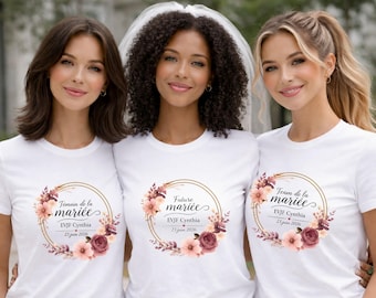 May include: Three women wearing white t-shirts with floral designs and text. The shirts have a gold circular frame with text in French, including "Témoin de la mariée", "Future mariée", and "Team de la mariée". The shirts also include the name "Cynthia" and the date "23 juin 2026".