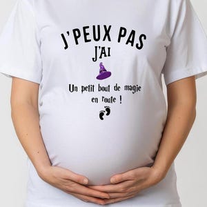 Può includere: Maglietta bianca con il testo "J'PEUX PAS J'AI Un petit bout de magie en route!" e un grafico di cappello da strega viola.