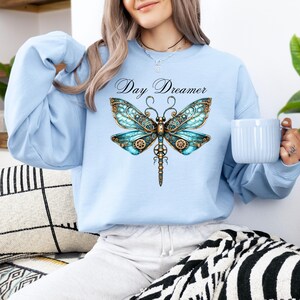 May include: Light blue sweatshirt with a graphic of a steampunk dragonfly and the text "Day Dreamer".