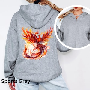 May include: A gray hooded sweatshirt with a colorful phoenix design on the back. The phoenix is depicted in a fiery orange and yellow color scheme with a watercolor effect. The sweatshirt has a zipper closure and a drawstring hood.