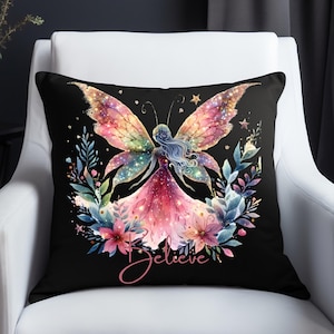 Puede incluir: Cojín decorativo negro con una ilustración de acuarela de un hada con alas de mariposa. El hada está rodeada de flores y follaje, con la palabra "Believe" en escritura cursiva.
