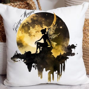 Op de afbeelding: Een wit kussen met een zwart en gouden aquarelontwerp van een fee die op een halve maan zit. De tekst "Fairy Magic" is geschreven in zwarte cursieve letters.