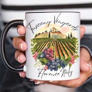May include: White ceramic mug with a black handle and rim, featuring a watercolor illustration of a Tuscan vineyard. The design includes a vineyard, a villa, and bunches of grapes, with the text "Tuscany Vineyards Florence Italy".