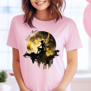 May include: A pink t-shirt with a graphic of a fairy sitting on a crescent moon with the text "Fairy Magic" printed on the shirt.