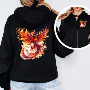 May include: Black zip-up hoodie with a phoenix design on the back. The phoenix is depicted in shades of orange, red, and yellow, with a watercolor effect. The text "Say what you will, but I'm a Phoenix" is printed on the back of the hoodie.