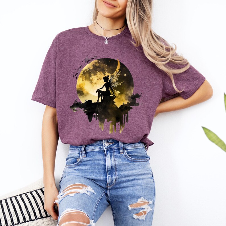 May include: A purple t-shirt with a graphic of a fairy sitting on a crescent moon with the words "Fairy Magic" in a black script font.