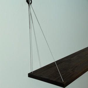 Op de afbeelding: Een donkerbruin houten plank die aan het plafond hangt met witte koorden bevestigd aan een zwarte haak.