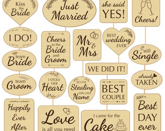 May include: A collection of wooden wedding photo booth props with various phrases like "Kiss the Bride," "Just Married," and "Cheers!" The props are light brown with dark brown text and decorative elements.