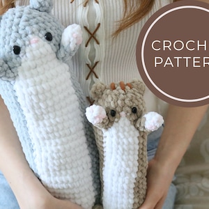 Może przedstawiać: Dwie szydełkowe zabawki dla kotów. Jedna jest jasnoszara i biała, druga beżowa i biała. Obie mają czarne oczy i różowe akcenty. Tekst "CROCHET PATTERN" znajduje się w brązowym okręgu.