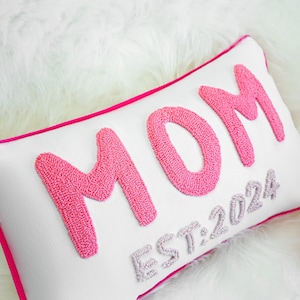 a pink and white pillow with the word mom on it