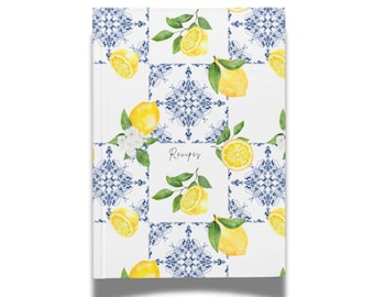 May include: A white recipe book with a pattern of blue and white tiles, lemons, and green leaves. The word "Recipes" is written in cursive. The cover features a watercolor design with a fresh, summery feel.