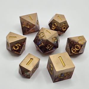 May include: Set of seven brown and gold dice with iridescent glitter embedded in the resin. The dice are numbered 1 through 6.