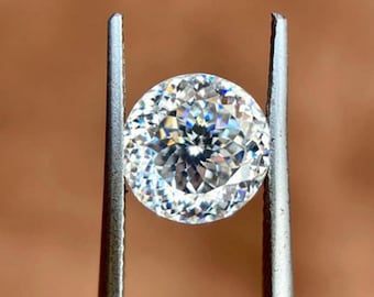 May include: A clear round gemstone with facets, held in place by two metal prongs.
