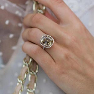 May include: A gold ring featuring a large, cushion-cut, champagne-coloured diamond encircled by a halo of smaller diamonds.