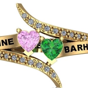 Puede incluir: Un anillo de oro con dos piedras preciosas en forma de corazón, una rosa y otra verde. El anillo tiene los nombres "MADELINE" y "BARHAM" grabados.