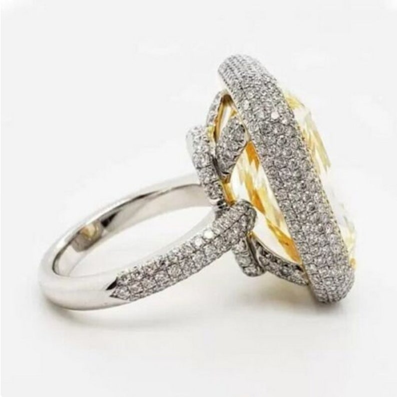 May include: A large, yellow, oval-shaped diamond ring set in a white gold band. The ring is surrounded by smaller diamonds, creating a halo effect.
